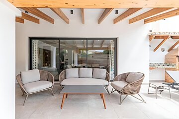 Modern patio with wicker furniture, a coffee table, and large sliding glass doors. Exposed wooden beams and a built-in outdoor kitchen complete the space.