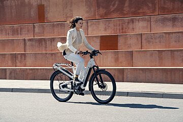 A woman in a white jacket is riding an electric bike