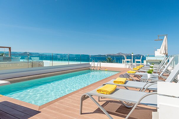 Rooftop pool deck with lounge chairs, yellow towels, and a beautiful blue ocean view under a clear sky.