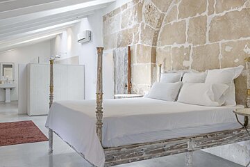 A bedroom with a four poster bed and a stone wall