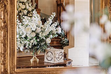 A vase of white flowers sits on a table next to a wooden box that says ' bride and groom ' on it
