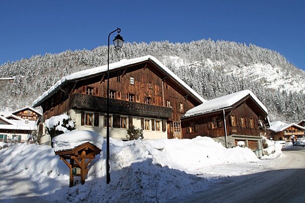 Rustic wooden chalets blanketed in snow, nestled against a backdrop of snow-dusted mountains under a clear blue sky.