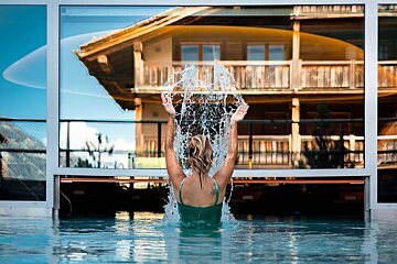 A woman is splashing water in a pool with a house in the background