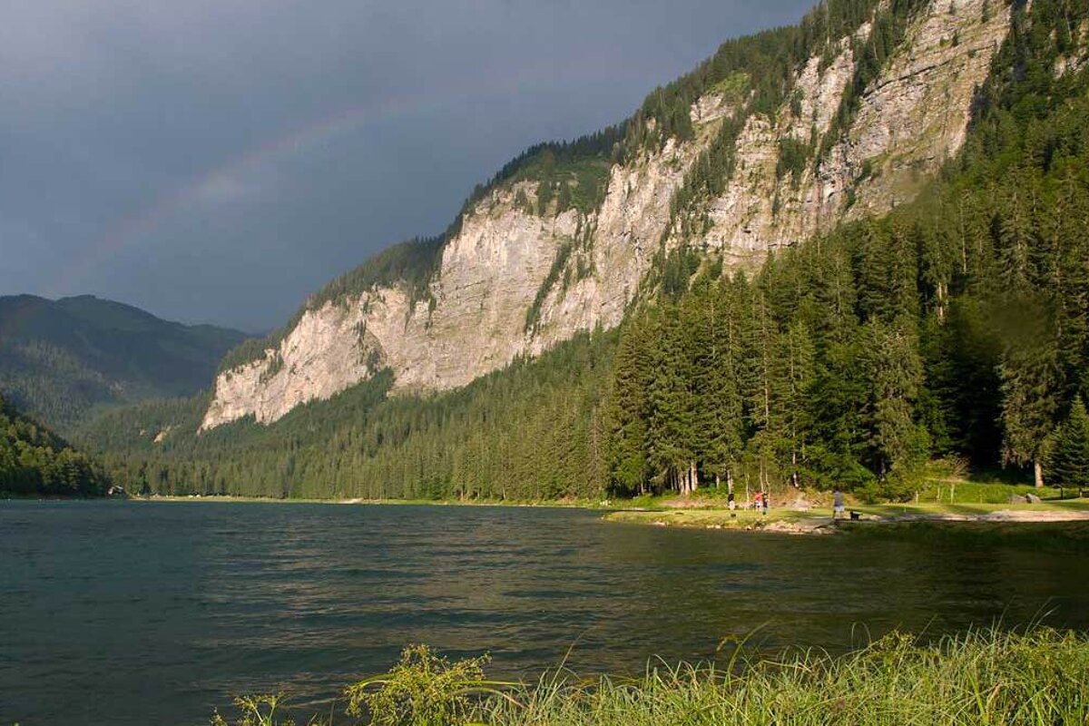 A lake surrounded by mountains and trees with a rainbow in the sky