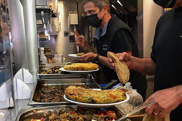 A man wearing a mask is serving food to another man