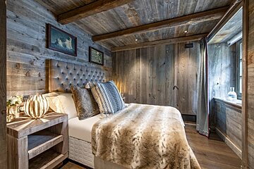 A bedroom with wooden walls and a bed with a fur blanket