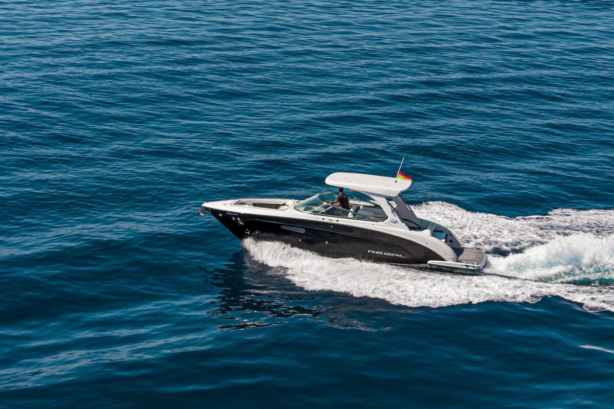 A sleek black and white motorboat cruises across deep blue water, leaving a trail of white wake.