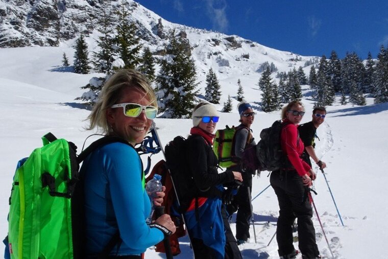 A woman wearing sunglasses stands in the snow holding a bottle of water