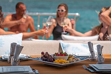 A plate of fruit sits on a table with people toasting in the background