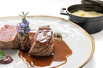 A white plate topped with meat and sauce next to a pot of mashed potatoes