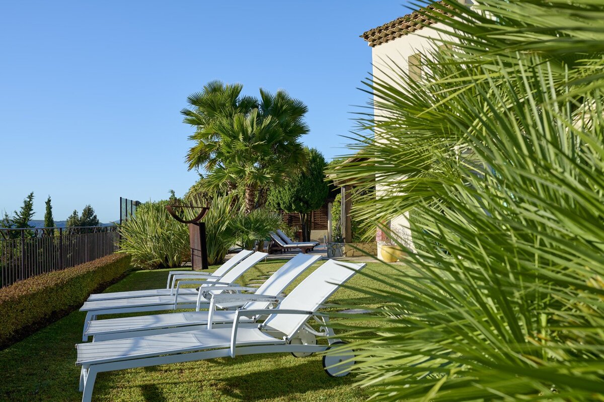 A row of white lounge chairs are lined up on a lush green lawn