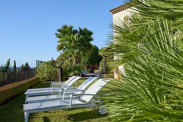 A row of white lounge chairs are lined up on a lush green lawn