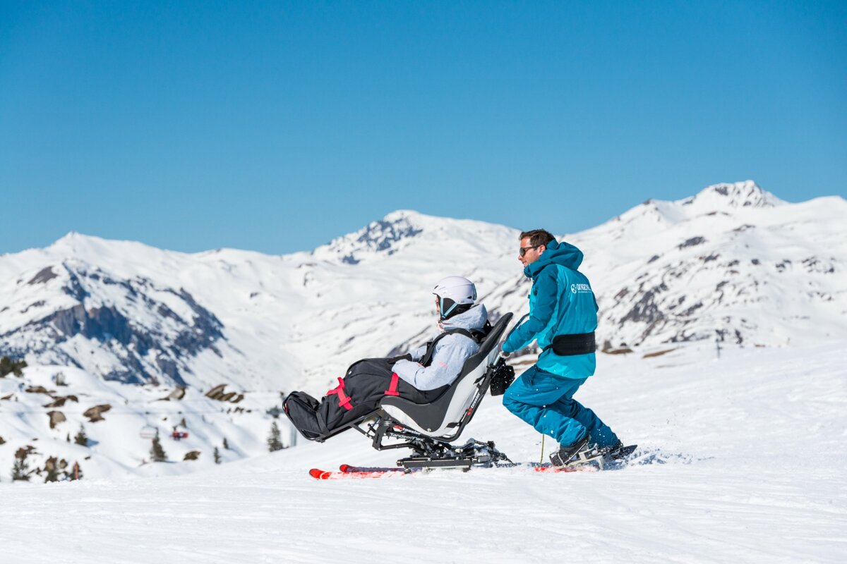 A person in a wheelchair is being pushed by a man wearing a jacket that says ' altitude ' on it