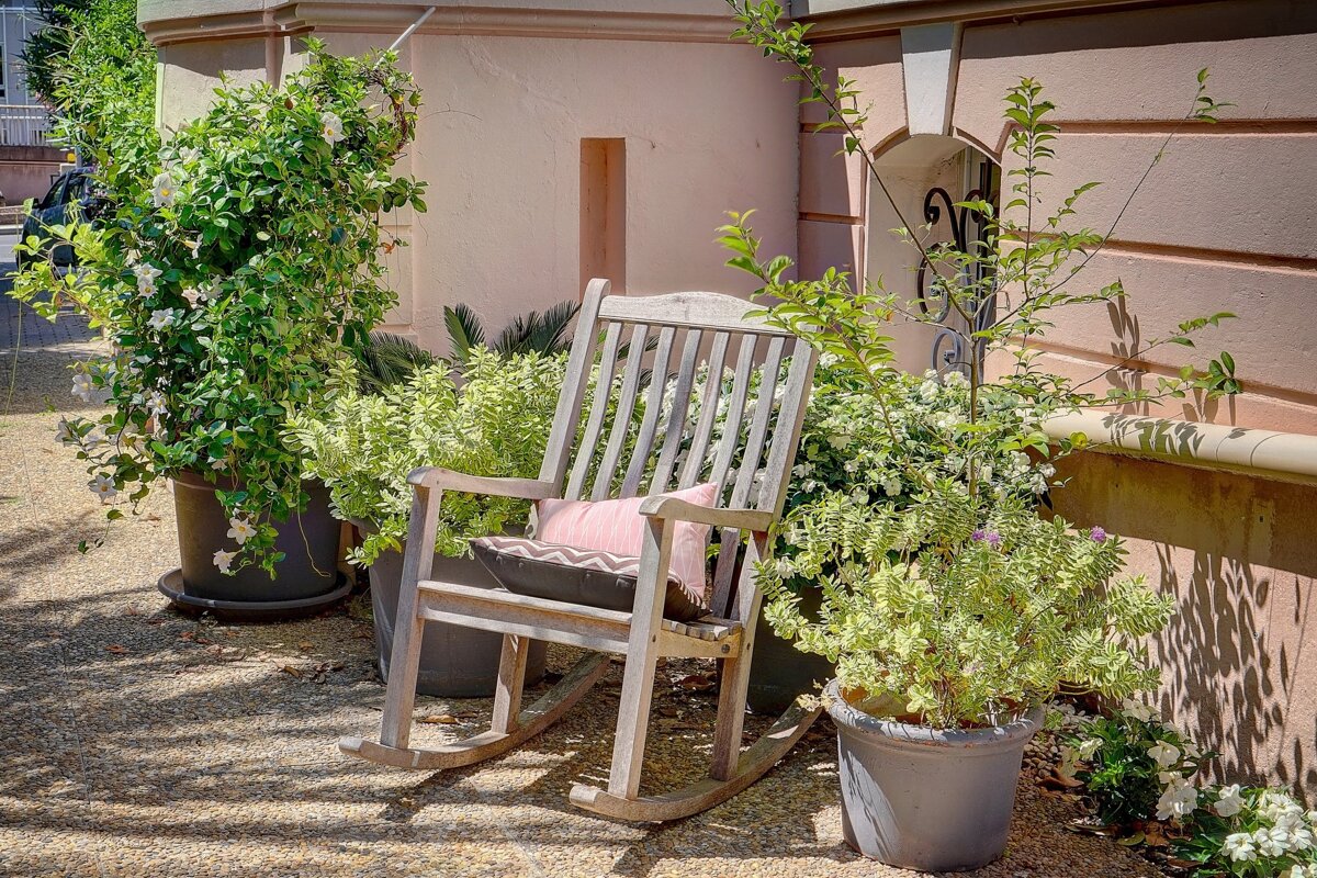 A rocking chair with a pink pillow sits in front of potted plants