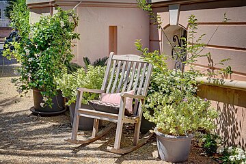 A rocking chair with a pink pillow sits in front of potted plants