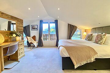 A bright, modern attic bedroom with a large bed, a desk, and a balcony offering scenic mountain views, creating a cozy and inviting space.