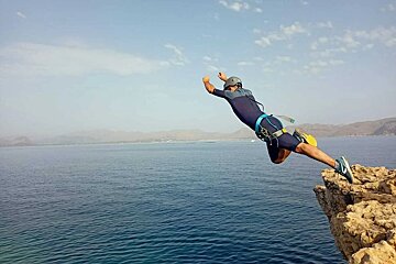 A man is jumping off a cliff into the ocean