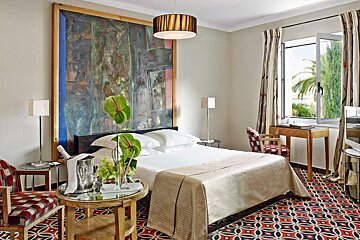 A bedroom with a large painting on the wall above the bed
