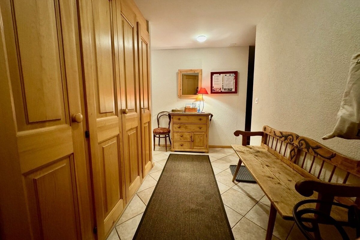 Rustic hallway with light wood cabinets, a dresser with a lamp and mirror, and a carved wooden bench on a tiled floor with a rug.