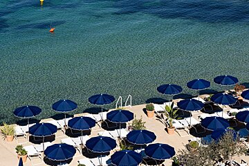 A row of blue umbrellas sit on a beach near the water
