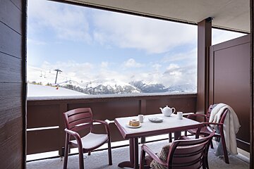A balcony with a table and chairs and a view of snowy mountains