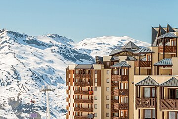 A ski lift going up a snowy mountain with a building in the foreground