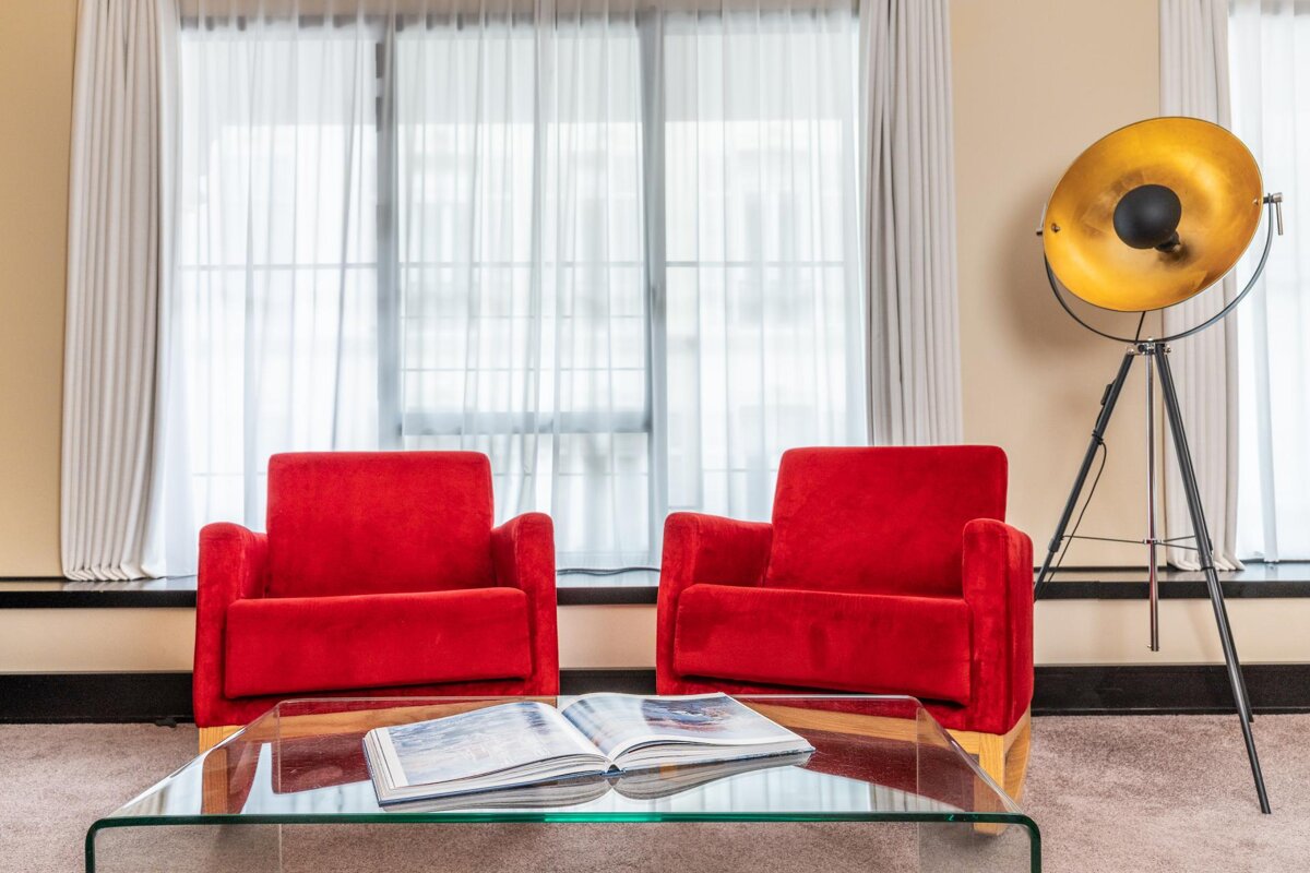 Two red chairs sit next to a glass coffee table with an open book on it