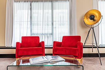 Two red chairs sit next to a glass coffee table with an open book on it