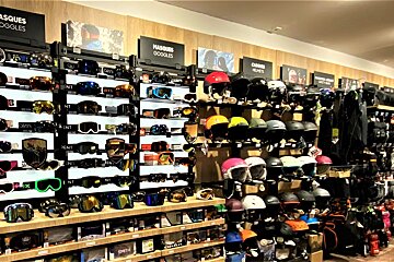 A retail store display features numerous ski goggles and helmets, showcasing a variety of styles and colors for winter sports enthusiasts.