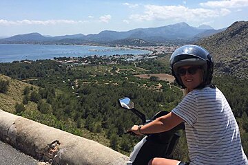 a girl on a moped with a view of the sea behind