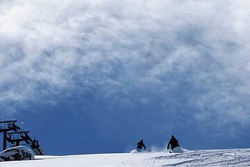 two skiers coming over a roller