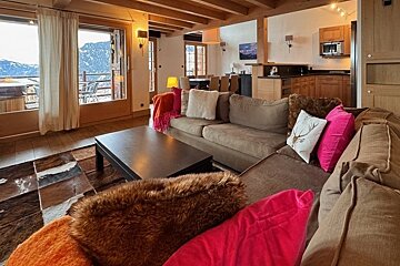 A cozy rustic cabin living room with a large sectional sofa, colorful throw pillows, and scenic mountain views.
