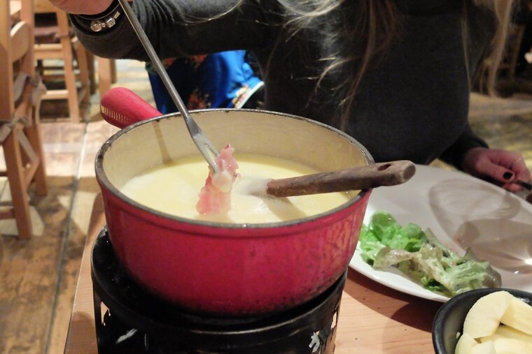 a small red fondue bowl with someone dipping meat into it