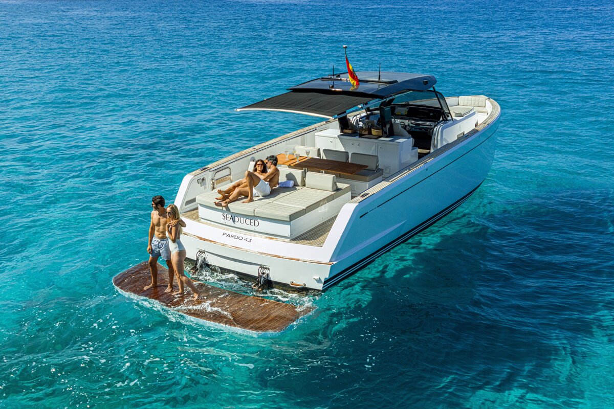 Four people relaxing on a luxury white yacht floating in crystal-clear turquoise ocean water.