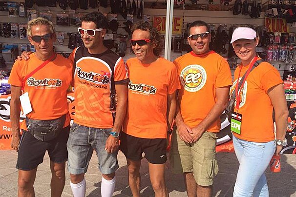 four men and one woman in orange t-shirt in front of a bike rental shop