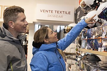 A man and a woman are looking at ski gear under a sign that says vente textile skiwear