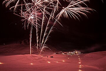 Fireworks are displayed in the night sky over a snowy area
