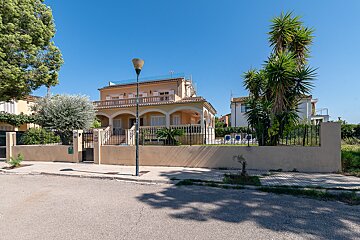 A large house is surrounded by a fence and palm trees