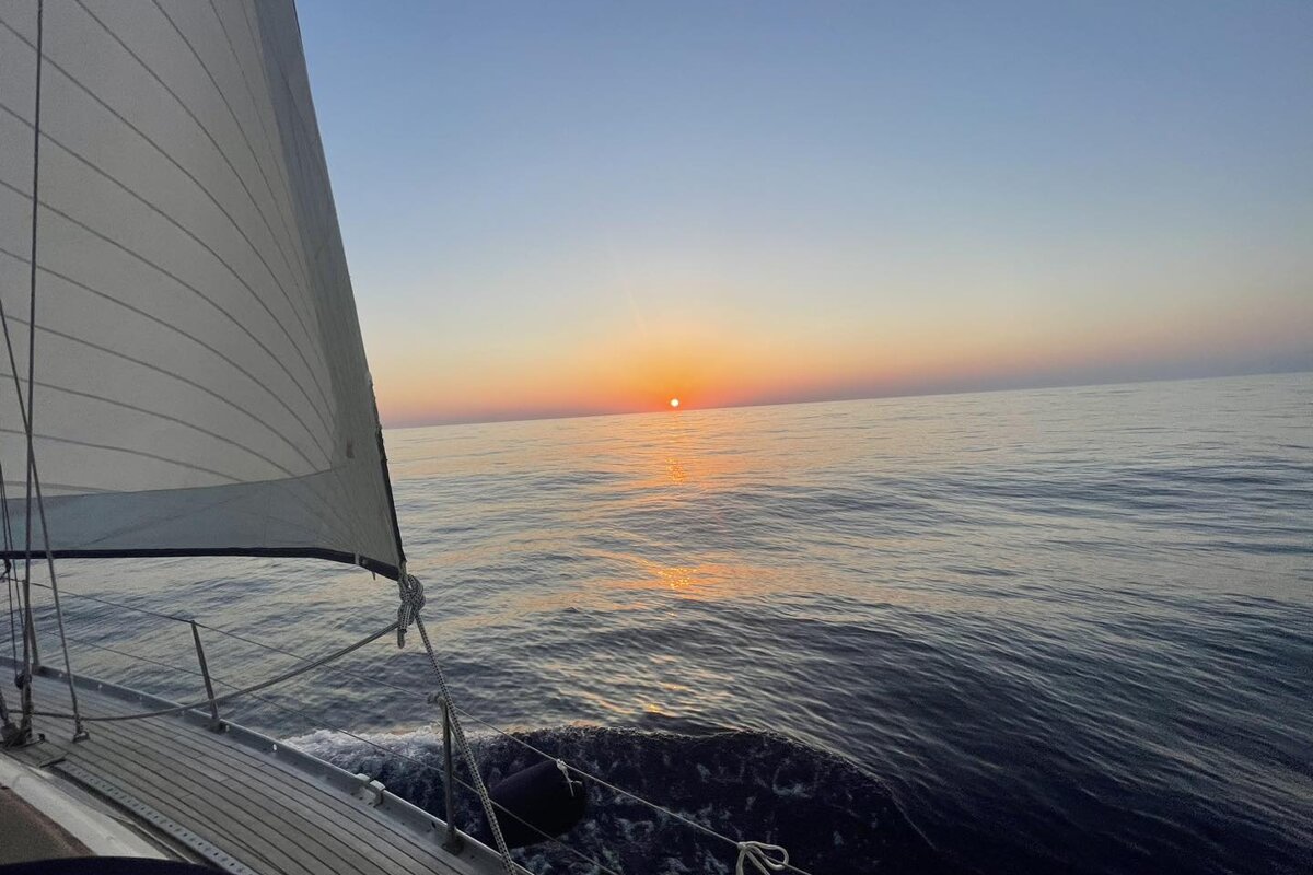 A sailboat is sailing in the ocean at sunset
