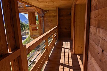 A wooden hallway with a balcony and mountains in the background