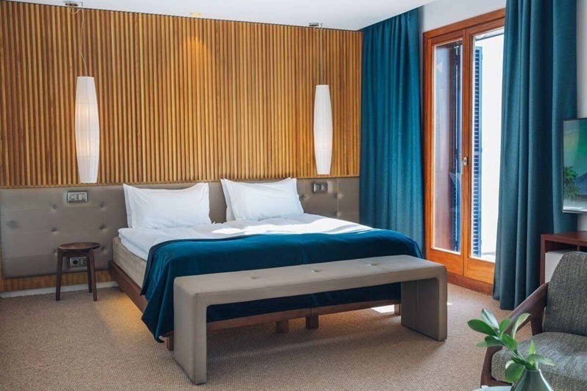 Stylish bedroom with a wooden slat accent wall, large bed with blue blanket, teal curtains, and a door leading to a balcony.