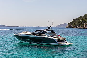 A sleek, modern yacht floats in crystal-clear turquoise water near a mountainous coastline under a sunny sky.