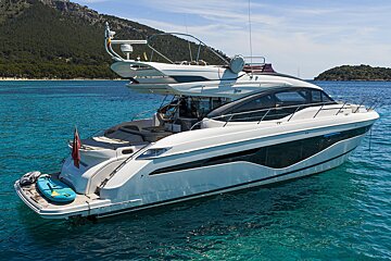 A white luxury yacht anchored in clear turquoise water with a mountainous coastline and clear blue sky in the background.
