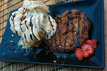 Cookie with ice cream and strawberries on black plate