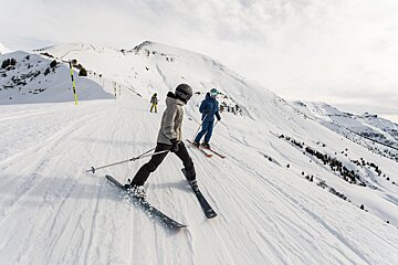 Skiers on a snowy slope with one wearing a gray jacket