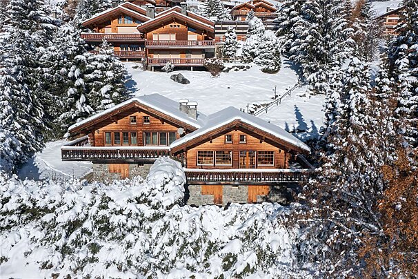 A large wooden house is surrounded by snow covered trees