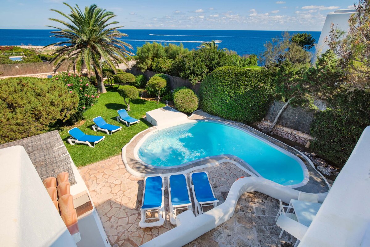 A swimming pool surrounded by blue chairs and palm trees with the ocean in the background