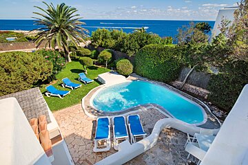 A swimming pool surrounded by blue chairs and palm trees with the ocean in the background