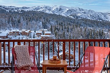 A bottle of beer sits on a table on a balcony overlooking snowy mountains