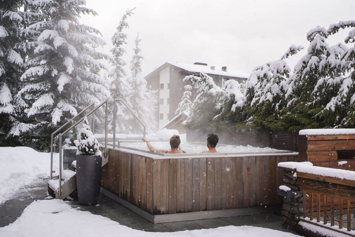 Two people in a hot tub surrounded by snow